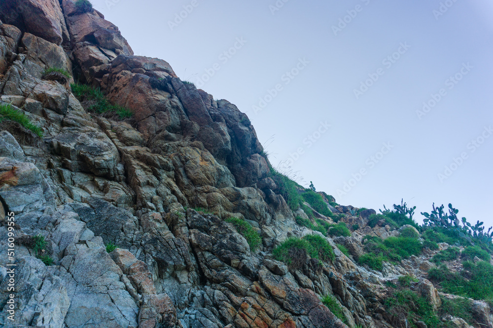 Fototapeta premium Rocky terrain with steep rough cliffs and scattered weeds. Mountain limestone rocks texture