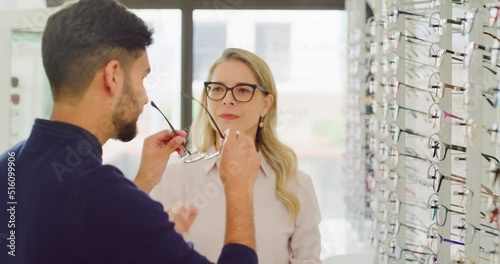 Female optician or optometrist helping a customer to choose glasses on the shelf in her shop. Friendly mature woman and owner helping a man to choose and try on spectacles in her optical store photo