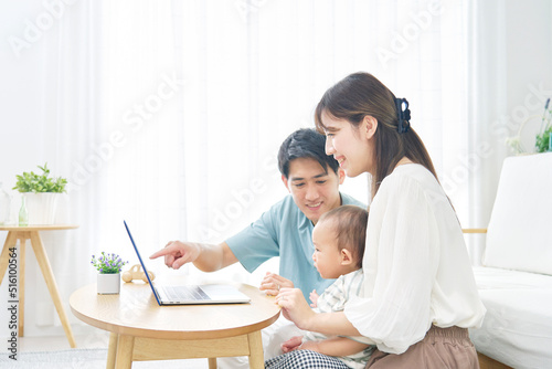 リビングで赤ちゃんとノートパソコンを見る両親
