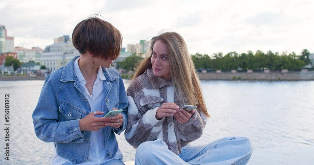 Normal life of a lesbian couple - women sit in an urban environment, surf on their phones and communicate nicely with each other. Normal life of a lesbian couple - women sit in an urban environment, surf on their phones and communicate nicely with each other.