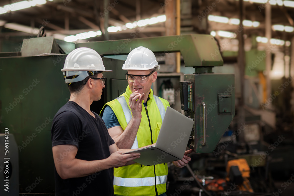 Two Caucasian Factory Technician Engineer wearing workwear safety uniform are working with machine in industrial plants and check the operation and maintenance program of the machine in the laptop. Two Caucasian Factory Technician Engineer wearing workwear safety uniform are working with machine in industrial plants and check the operation and maintenance program of the machine in the laptop.
