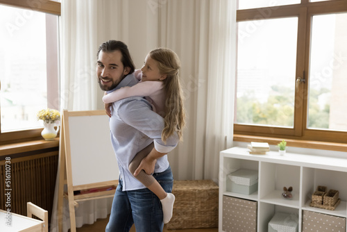 Happy joyful young dad piggybacking little daughter kid, dancing in playroom, walking, carrying girl on back, having fun, enjoying activity, playing games at home. Fatherhood, family playtime concept