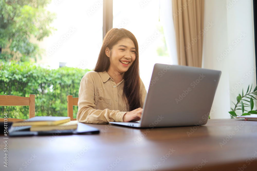 Asian woman using laptop with smiling face on her desk in office showing positive attitude about full-time work and being a successful person. Asian woman using laptop with smiling face on her desk in office showing positive attitude about full-time work and being a successful person.