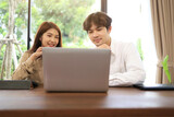 A woman and a man sit and look at laptop screens on their desks in the office in a relaxed and good mood.