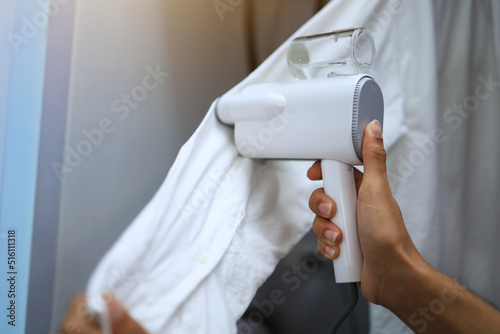 Close up shot asian man is using a steamer to flatten his clothes before going to work.