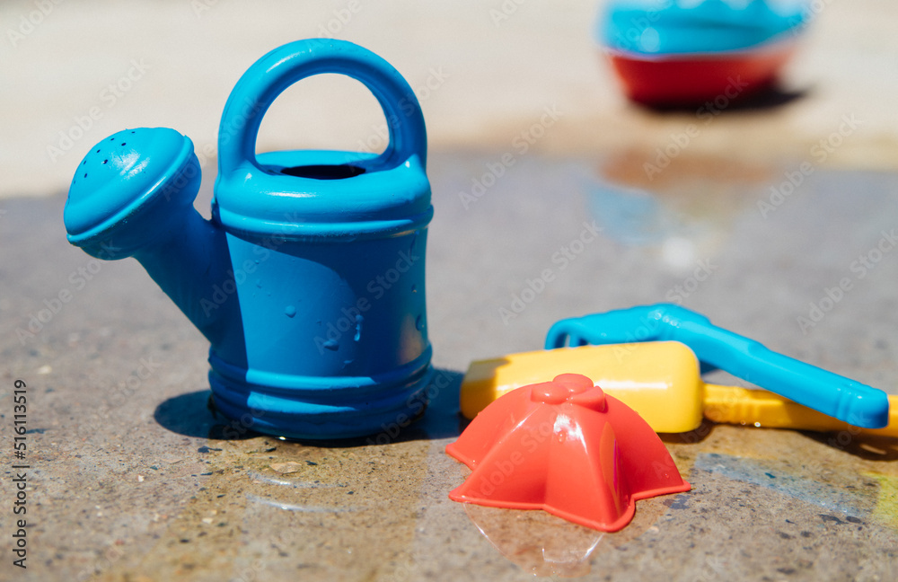 A set of children's toys for playing in the sandbox. Colored rake, shovel, watering can made of plastic, close-up. Early development of the child, the concept of children's leisure. A set of children's toys for playing in the sandbox. Colored rake, shovel, watering can made of plastic, close-up. Early development of the child, the concept of children's leisure.