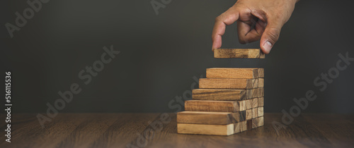 Hand placing wooden block tower stack in pyramid stair step with caution to prevent collapse or crash concepts of financial risk management and strategic planning and business challenge plan.