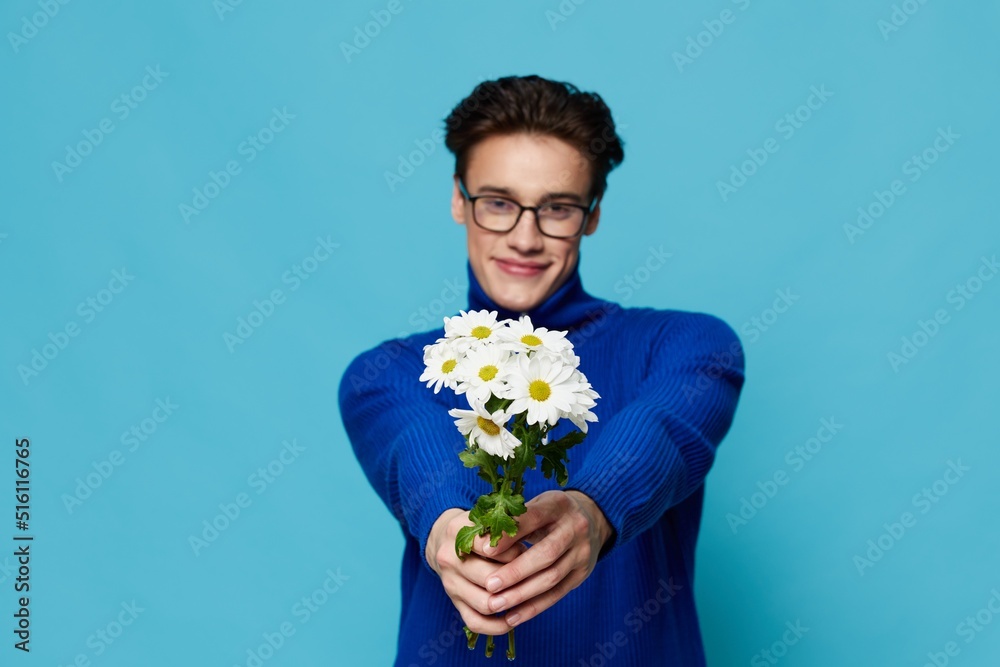 a horizontal portrait of a cute man in black eyeglasses and a blue zip-up sweater, holding out a bouquet of white daisies to the camera with a wide smile on his face a horizontal portrait of a cute man in black eyeglasses and a blue zip-up sweater, holding out a bouquet of white daisies to the camera with a wide smile on his face