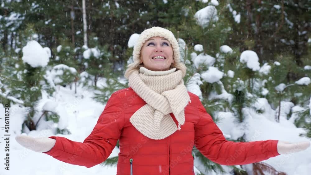 Woman plays with snow. Lady wearing red jacket and white hat with scarf walks across trees and enjoys life and smiles. Woman looks around, closeup Woman plays with snow. Lady wearing red jacket and white hat with scarf walks across trees and enjoys life and smiles. Woman looks around, closeup