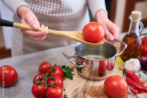 woman blanching a tomato holding over pan with hot water for further peeling photo