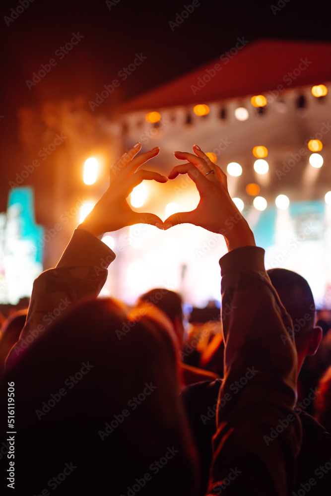 Heart shaped hands at concert, loving the artist and the festival. Music concert with lights and silhouette of people enjoying the concert. - obrazy, fototapety, plakaty 