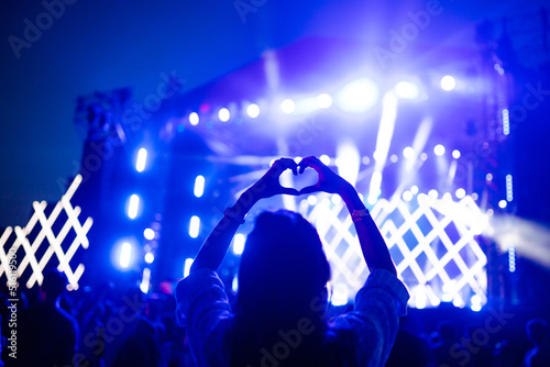 Heart shaped hands at concert, loving the artist and the festival. Music concert with lights and silhouette of people enjoying the concert. photo