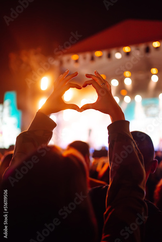 Heart shaped hands at concert, loving the artist and the festival. Music concert with lights and silhouette of people enjoying the concert.