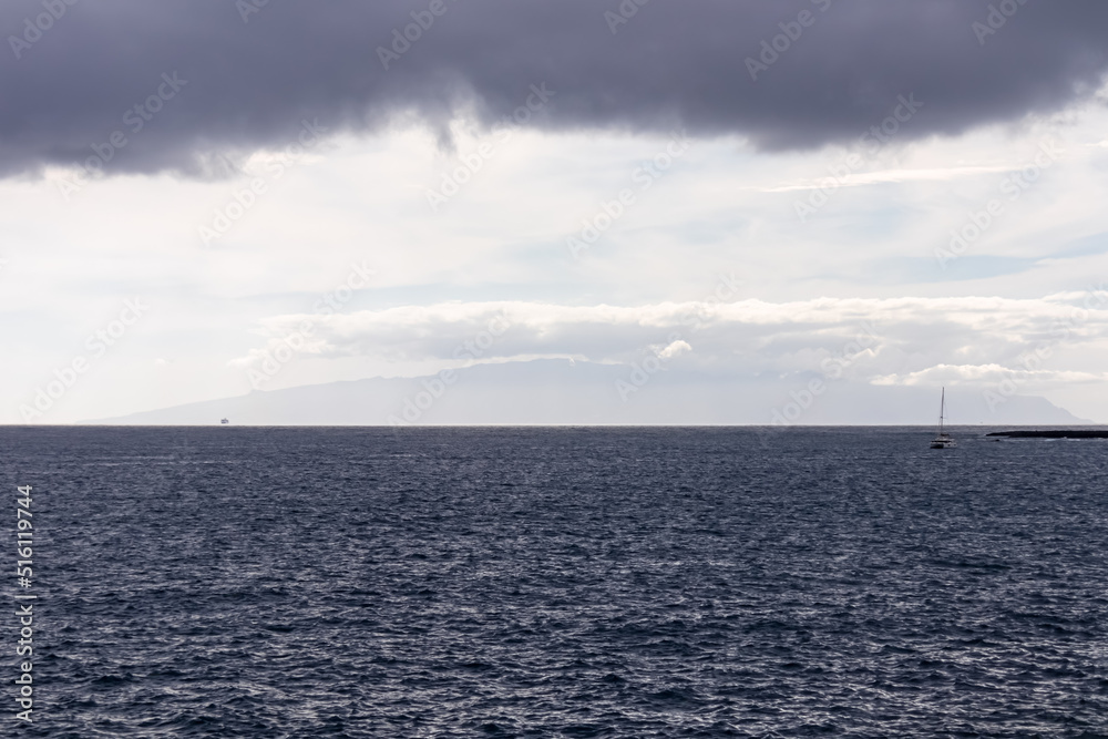 Panoramic open sea view seen from Abades beach in Poris de Abona on the east coast of Tenerife, Canary Islands, Spain. Very dark rain clouds coming from the back. Small sailing boat in the distance Panoramic open sea view seen from Abades beach in Poris de Abona on the east coast of Tenerife, Canary Islands, Spain. Very dark rain clouds coming from the back. Small sailing boat in the distance