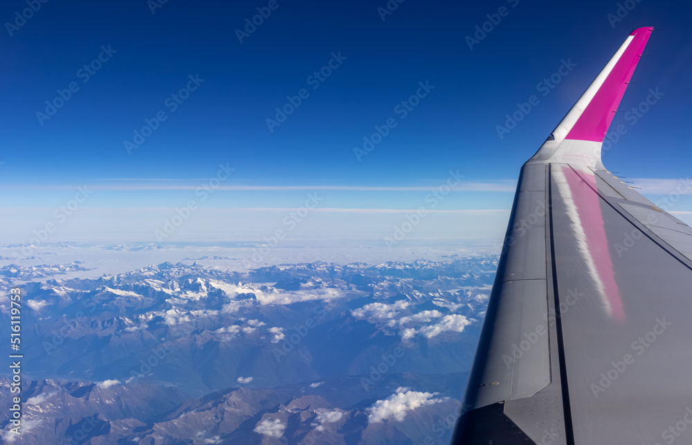 Window view from an airplane on snow capped mountain ranges of the Austrian Italian Alps Europe. High peak are shrouded in clouds. Wing of the plane in corner. Flying high above the ground. Freedom Window view from an airplane on snow capped mountain ranges of the Austrian Italian Alps Europe. High peak are shrouded in clouds. Wing of the plane in corner. Flying high above the ground. Freedom