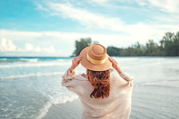 Summer beach vacation concept, Young woman with hat relaxing with her arms raised to her head enjoying looking view of beach ocean on hot summer day, copy space.