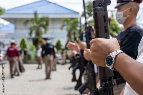A close-up view of the arm of a Thai policeman, adorned with a wristwatch, is carrying an antique wooden long-barrelled gun.