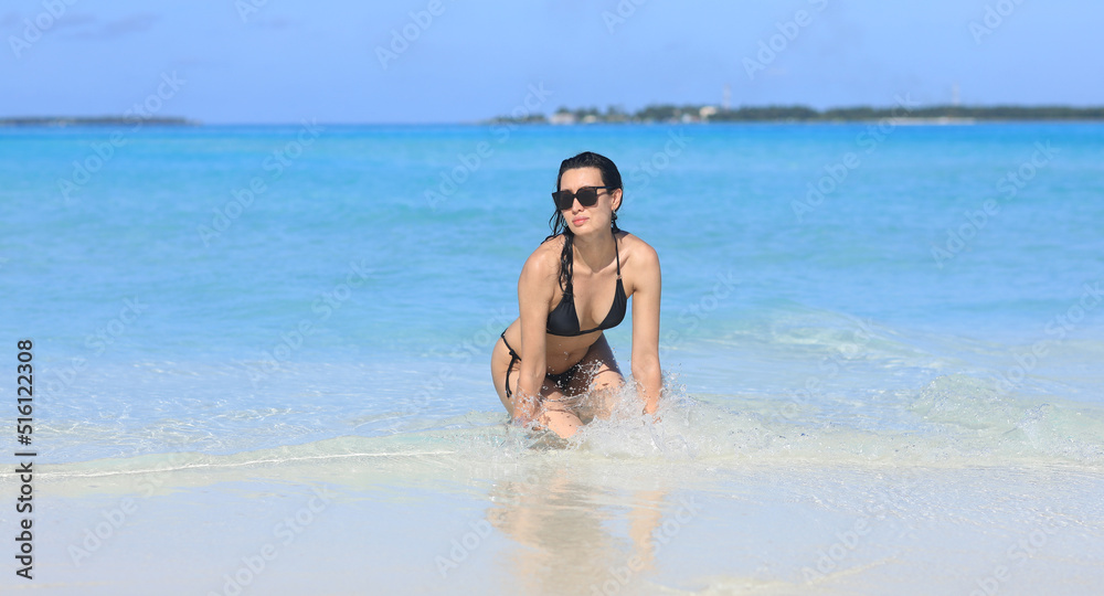 girl model in a black bikini on the white sand by the ocean