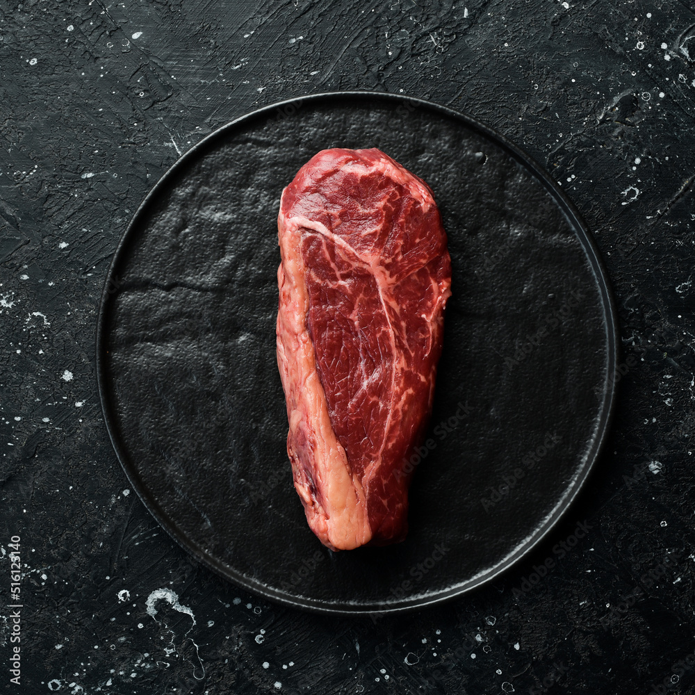 Classic raw New York beef steak. Fresh meat with seasonings. Aged steak. Top view. On a black stone background.