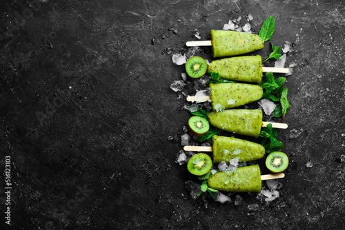 summer popsicles with ice and kiwi. On a black stone background.