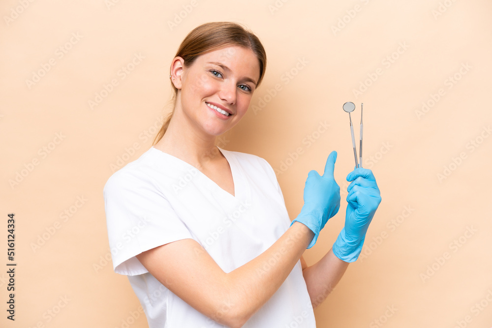 Dentist caucasian woman holding tools isolated on beige background pointing back Dentist caucasian woman holding tools isolated on beige background pointing back