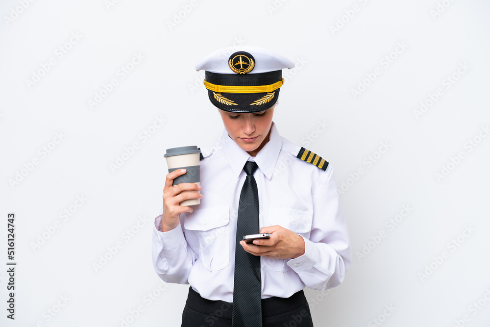 Airplane caucasian pilot woman isolated on white background holding coffee to take away and a mobile
