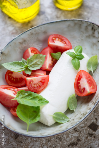 Close-up of mozzarella cheese with tomato wedges and fresh green basil served in a grey bowl, vertical shot, selective focus