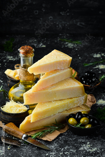 Hard cheese with olives and cheese knife on black stone background. Parmesan. Top view. Free space for your text.