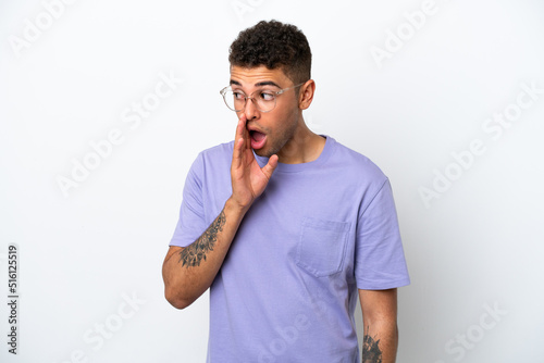 Young caucasian Brazilian man isolated on white background whispering something with surprise gesture while looking to the side