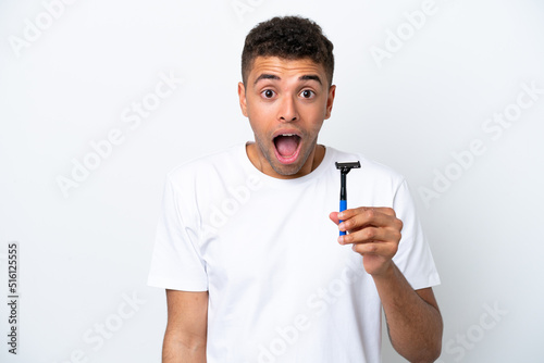Young Brazilian man shaving his beard isolated on white background with surprise and shocked facial expression