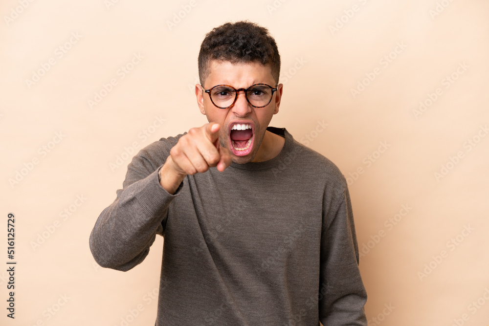 Young Brazilian man isolated on beige background frustrated and pointing to the front Young Brazilian man isolated on beige background frustrated and pointing to the front