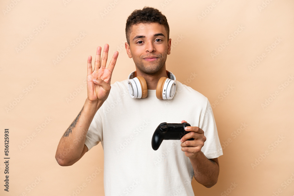 Young Brazilian man playing with a video game controller isolated on beige background happy and counting four with fingers Young Brazilian man playing with a video game controller isolated on beige background happy and counting four with fingers