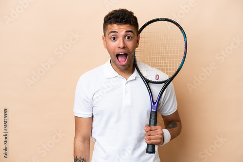Young brazilian handsome man playing tennis isolated on beige background with surprise facial expression © luismolinero