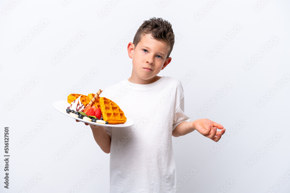 Little caucasian boy holding a waffles isolated on white background making doubts gesture while lifting the shoulders Little caucasian boy holding a waffles isolated on white background making doubts gesture while lifting the shoulders