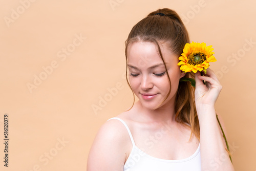 Young caucasian girl isolated on beige background holding a sunflower. Close up portrait