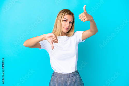 Blonde Uruguayan girl isolated on blue background making good-bad sign. Undecided between yes or not