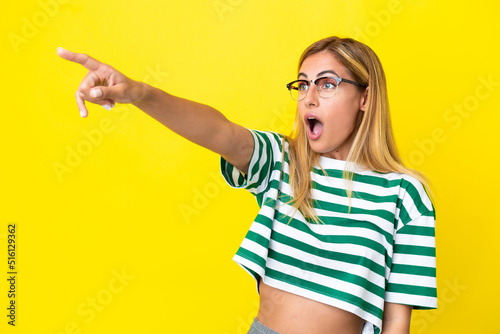 Blonde Uruguayan girl isolated on yellow background pointing away