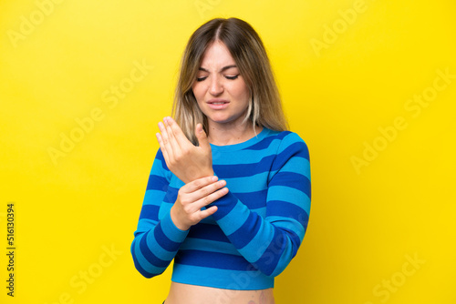 Young Rumanian woman isolated on yellow background suffering from pain in hands