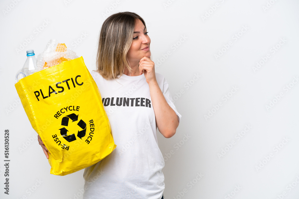 Young Rumanian woman holding a recycling bag full of plastic to recycle isolated on white background thinking an idea and looking side Young Rumanian woman holding a recycling bag full of plastic to recycle isolated on white background thinking an idea and looking side