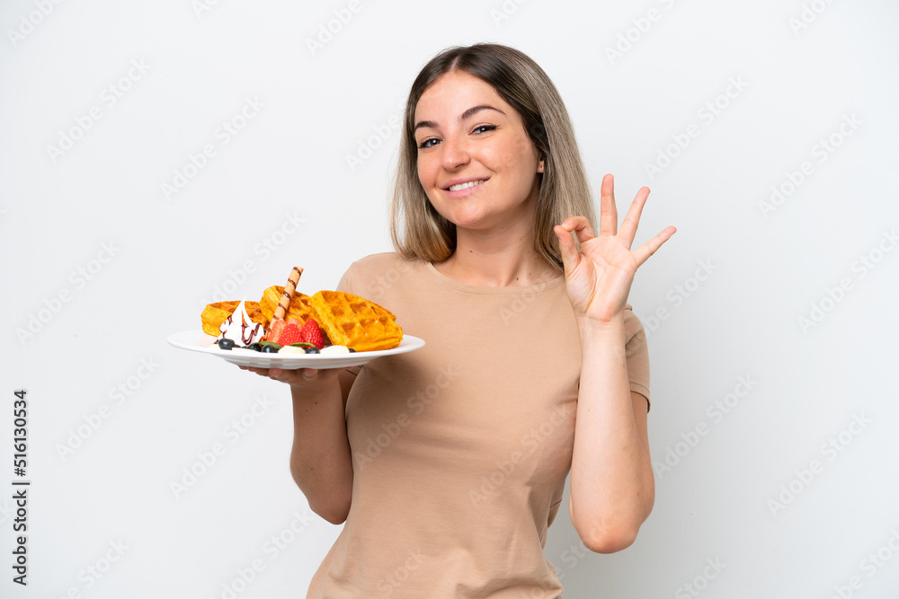 Young Rumanian woman holding waffles isolated on white background showing ok sign with fingers Young Rumanian woman holding waffles isolated on white background showing ok sign with fingers