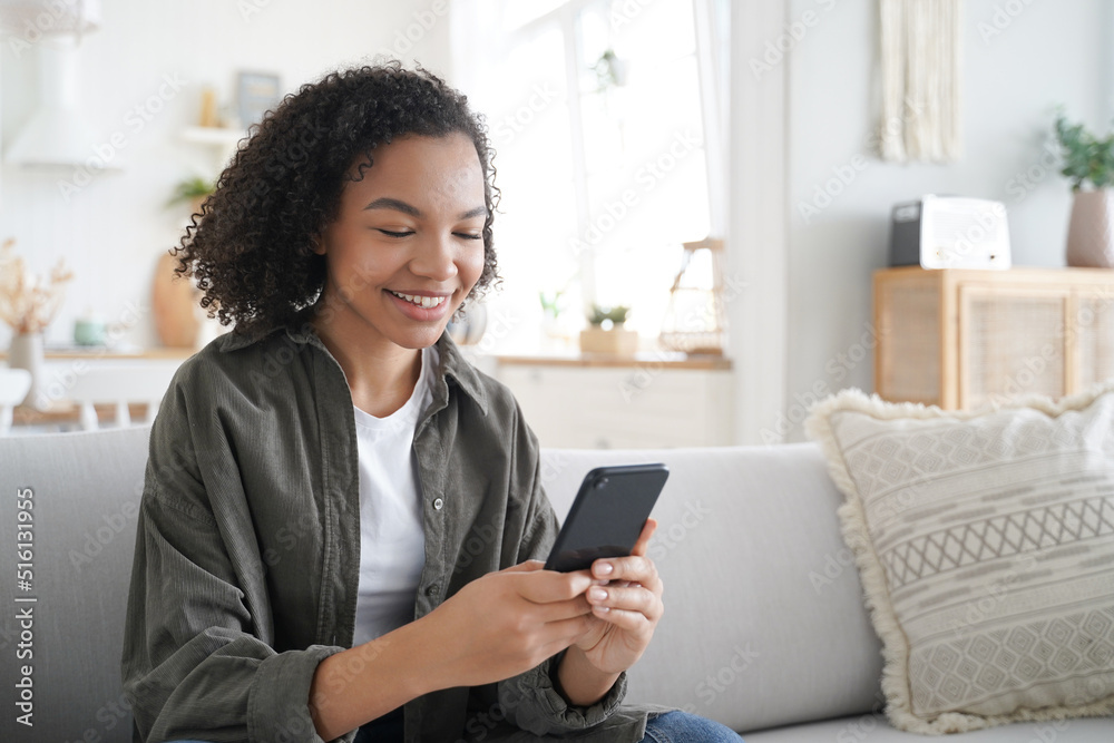 Curly african american girl has fun with phone at home and smiling. Communication concept. Curly african american girl has fun with phone at home and smiling. Communication concept.