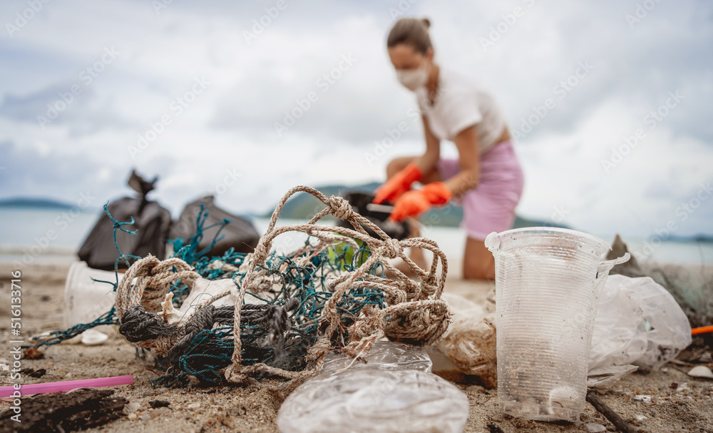 Obraz premium A female ecologist volunteer cleans the beach on the seashore from plastic and other waste
