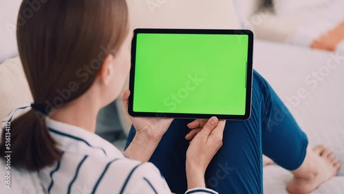 unrecognizable woman sitting on a couch wearing casual shirt and blue trousers using digital tablet with green screen leisure time at home