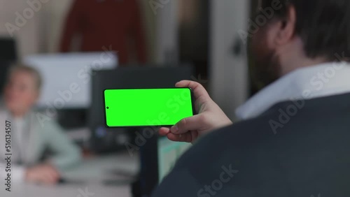 Back view of male manager looking at smartphone green screen sitting in office