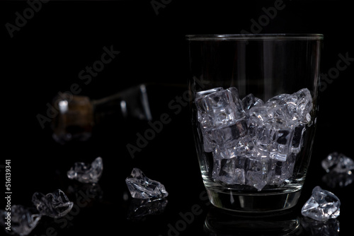 Empty glass filled with ice cubes on black background