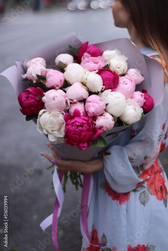 A large bouquet of white and pink peonies in the hands of a girl in a blue dress without a face