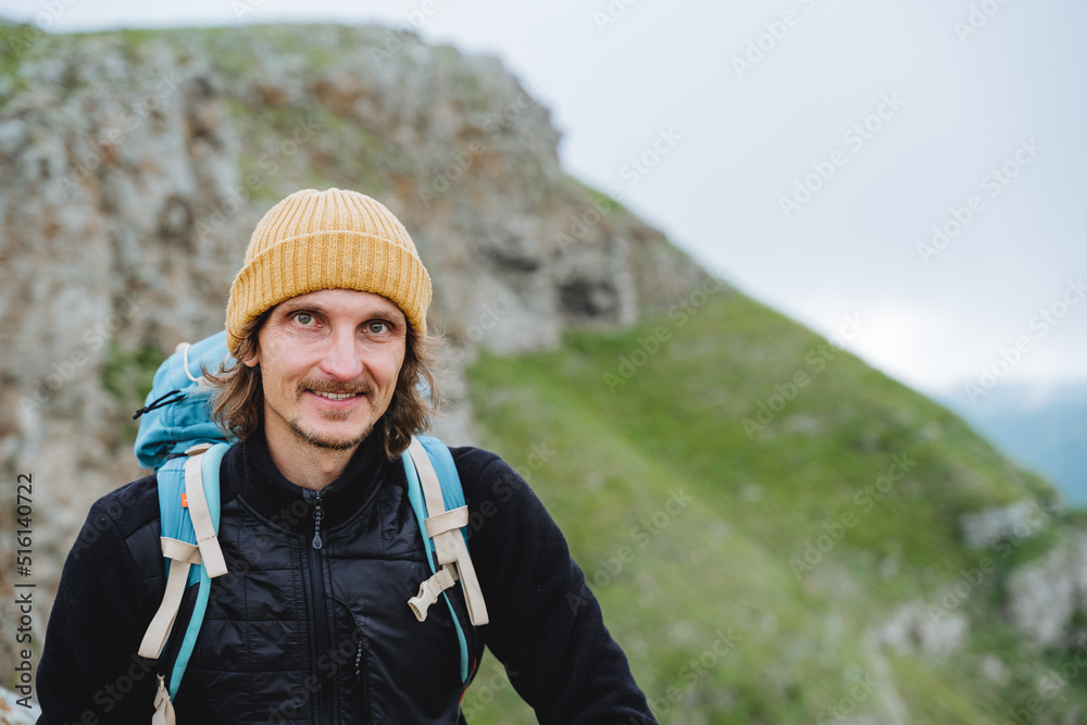 Portrait of a guy in the mountains, a man smiling looks at the camera, a man in a yellow hat in nature, a tourist with a backpack in the mountains, a mountain hike, a smile on his face