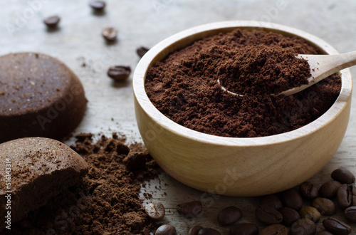ground coffee in a wooden bowl on concrete background with a pile of arabica coffee beans.
