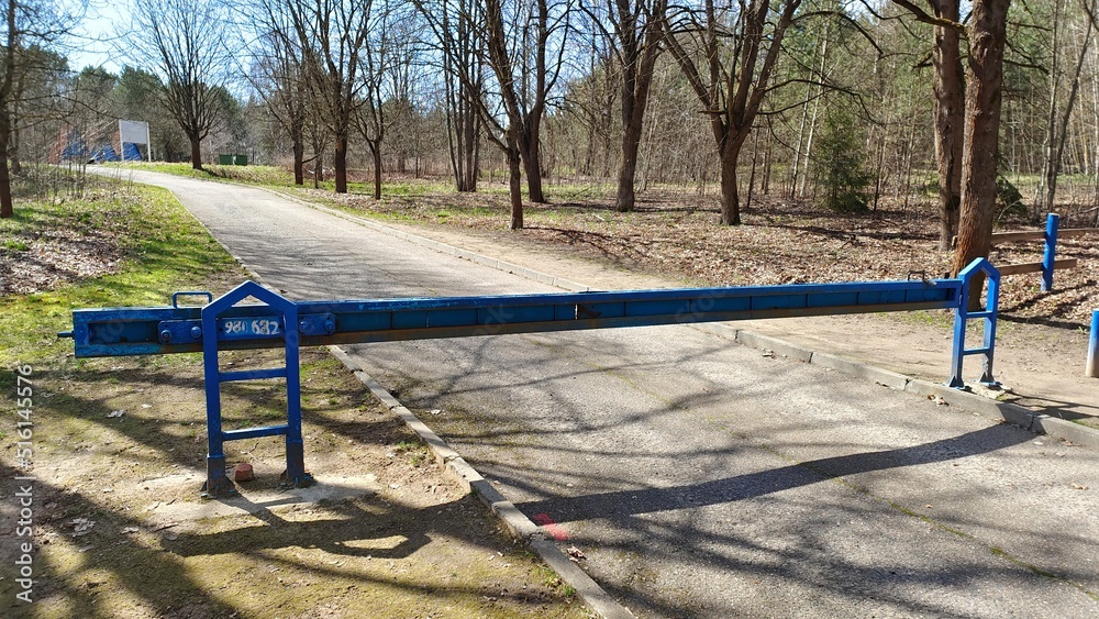 On the asphalt road leading to the recreation area, installed rolling metal barrier. On the sides of the road grows a forest. The weather is sunny On the asphalt road leading to the recreation area, installed rolling metal barrier. On the sides of the road grows a forest. The weather is sunny
