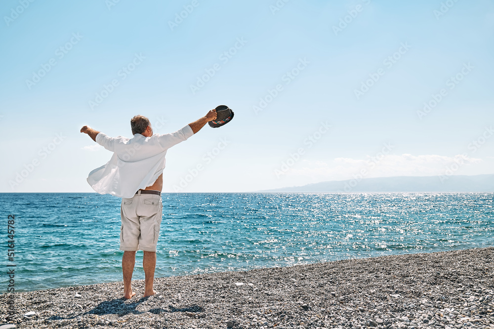 Happy middle-aged tourist man enjoying freedom with open hands on sea. Wellness, success, freedom and travel concept. Trip in summertime.